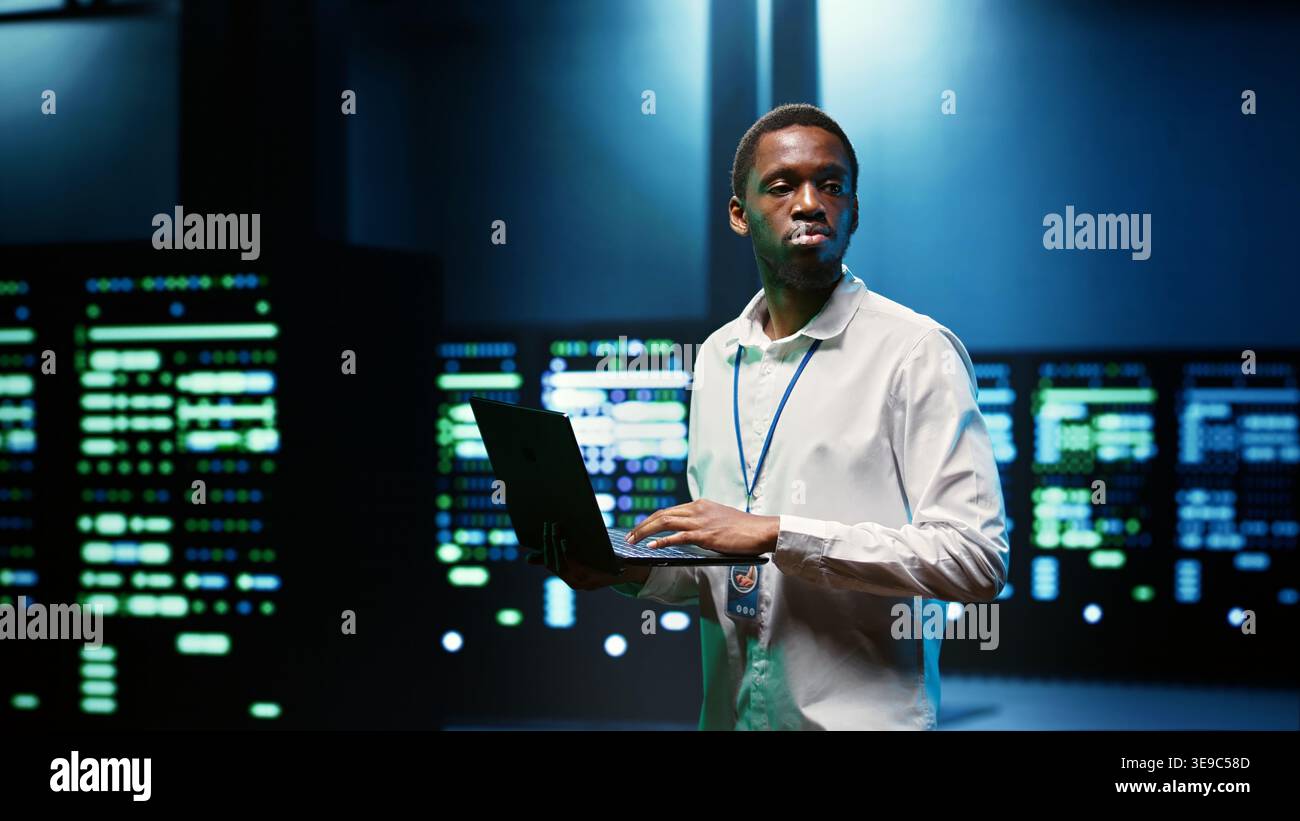 IT developer in server room using laptop to find network issues affecting supercomputer performance and connectivity, leading to slow data transfer rates and poor client communication Stock Photo