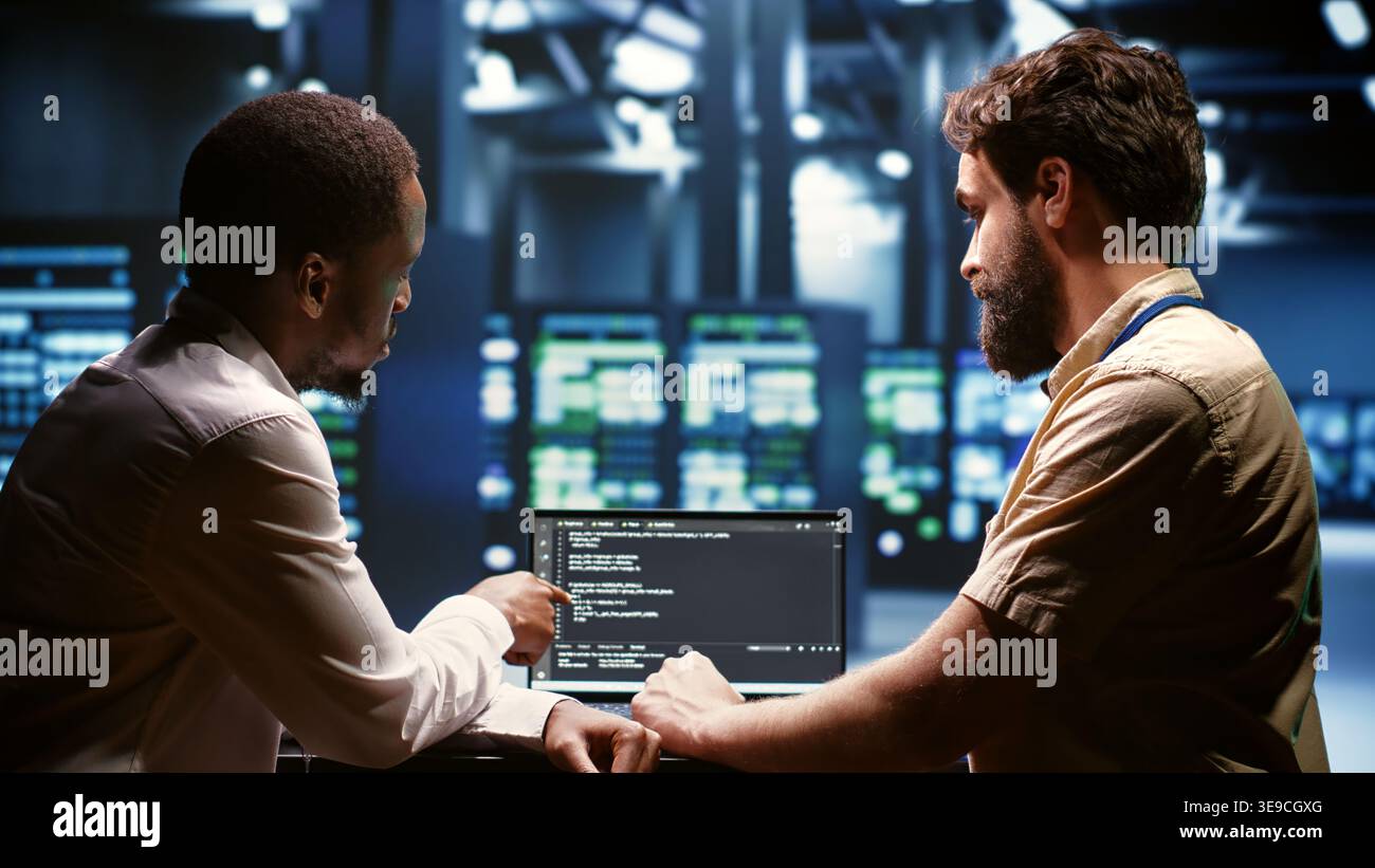 IT developers team writing server script code in data center on laptop terminal. Teamworking programmers doing maintenance work in high tech facility updating rigs software Stock Photo