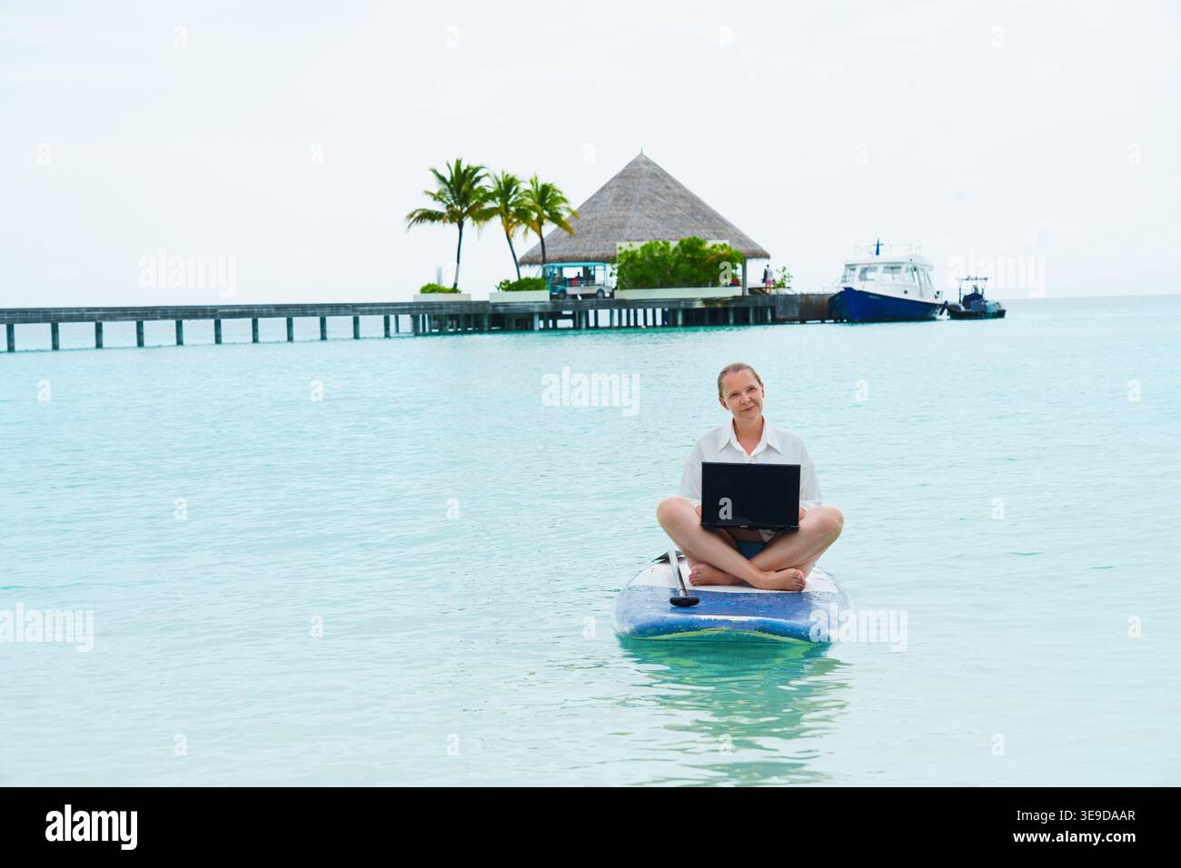 Smiling, successful woman with laptop surfing on a SUP  Success. Flexible remote work, female work-life balance concept. Stock Photo
