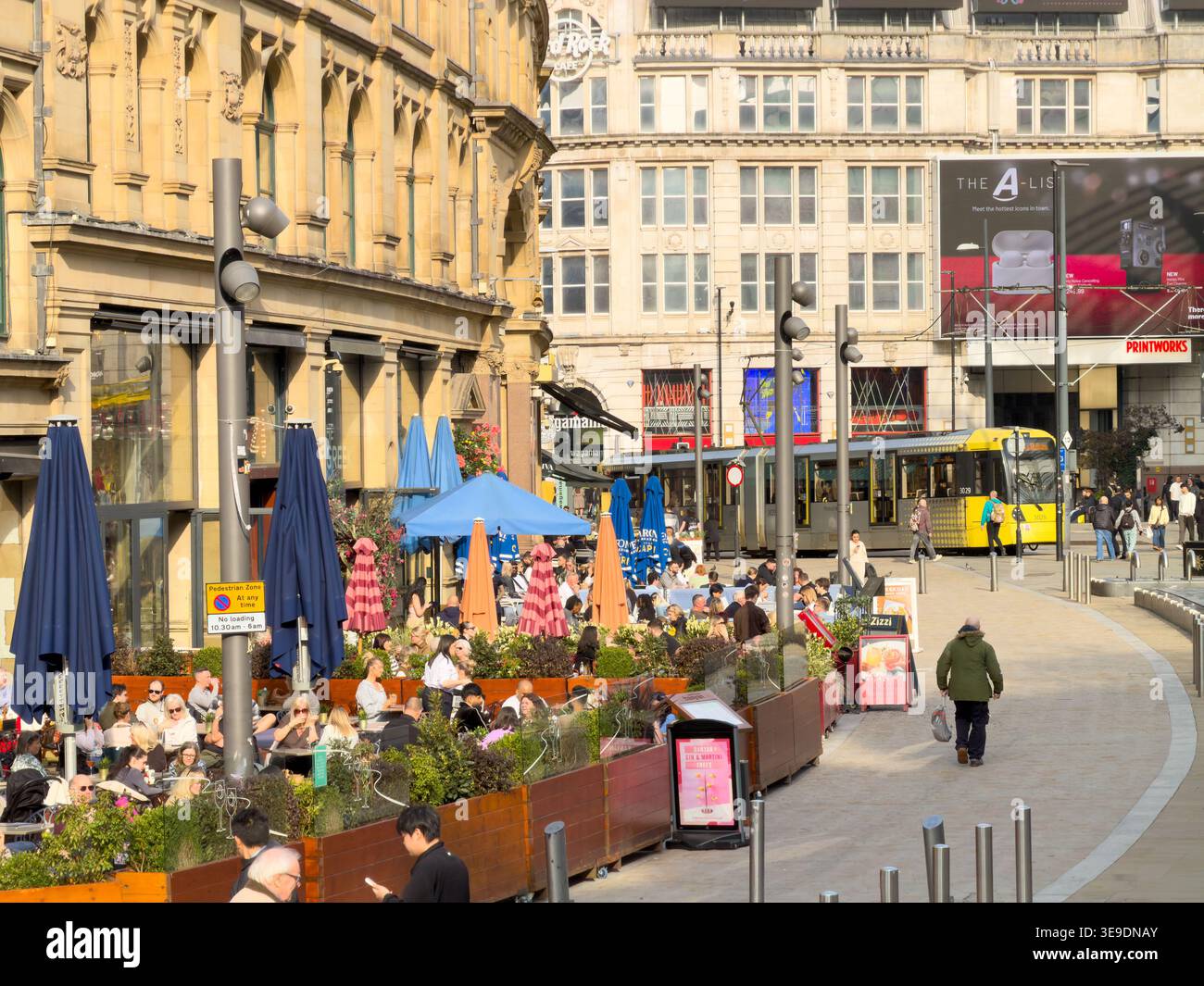 MANCHESTER, GREATER MANCHESTER, ENGLAND - MARCH 19, 2026: People sit at outdoor cafes, Printworks entertainment complex in Manchester, as Metrolink tr Stock Photo