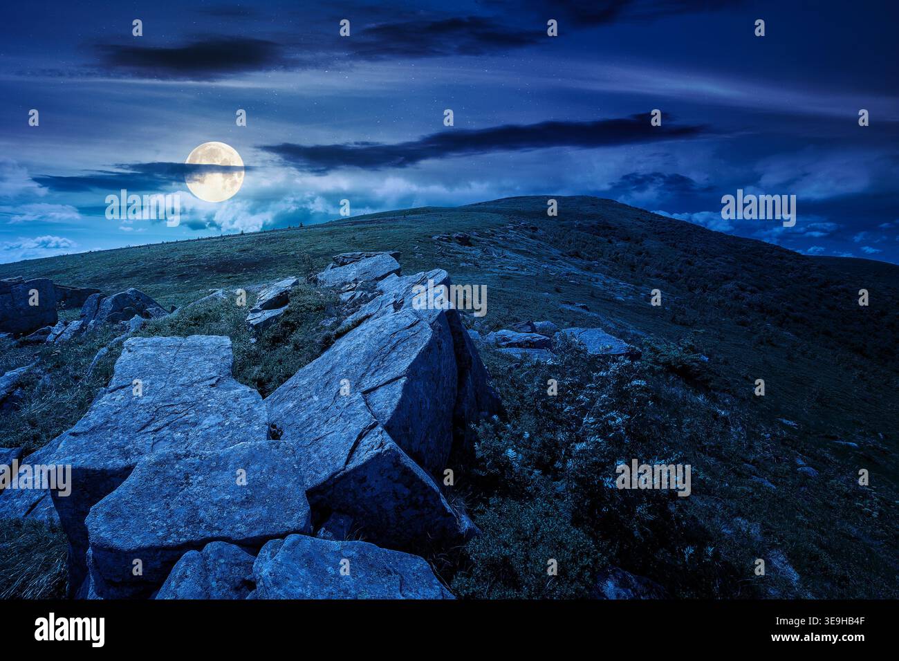 rocks and rolling hills in mountain landscape in summer at night. full moon over scenery with green grass on alpine meadow under dark sky with clouds. Stock Photo