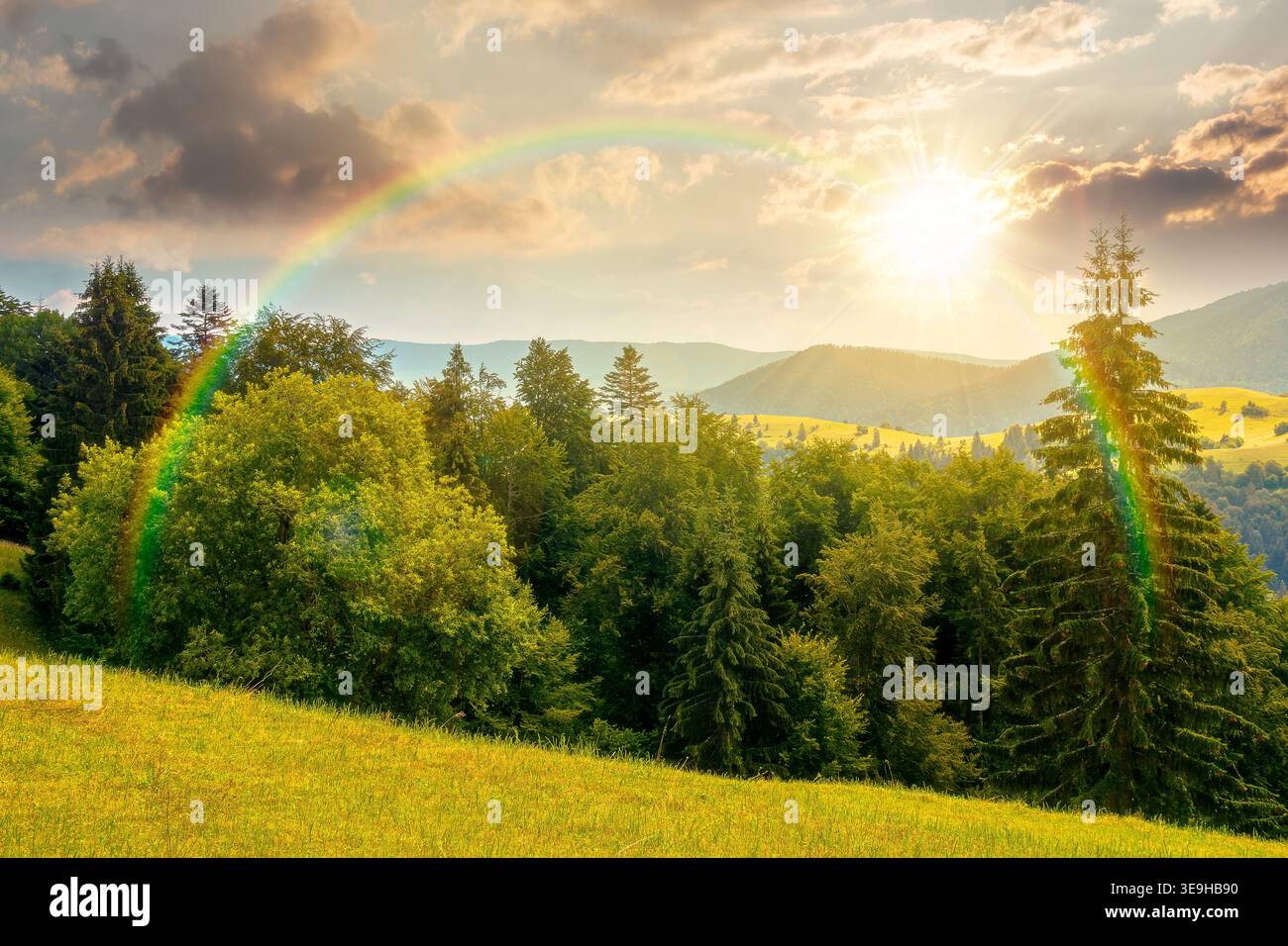sunset over mountain hay field. alpine countryside summer landscape with green valley behind the woods on the grassy slope. cloudy sky. spectacular hi Stock Photo