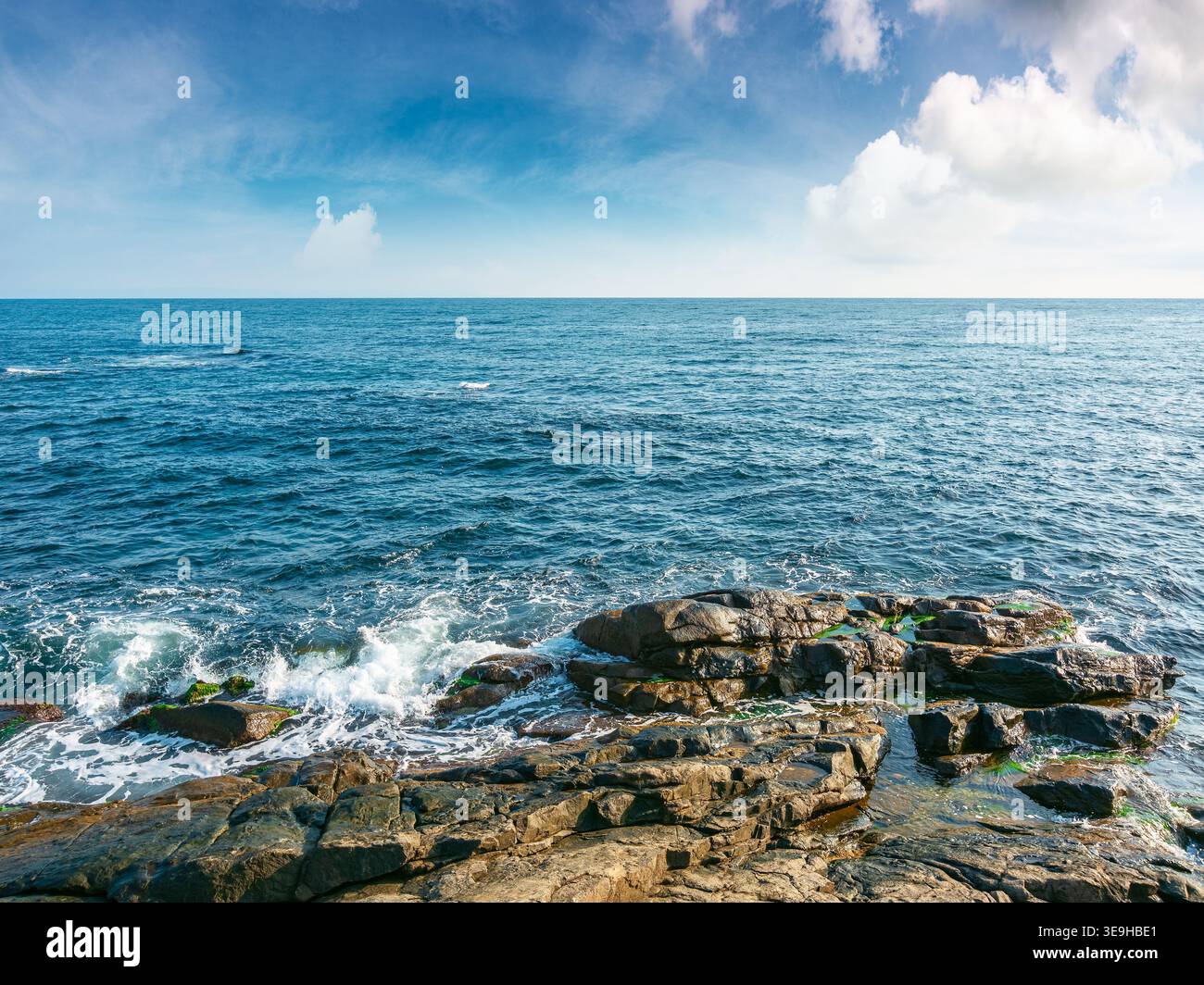 sea coast with stones and boulders in the forenoon. view of beach with rock in seaweed. dynamic cloudscape on the sky over horizon. summer vacations b Stock Photo