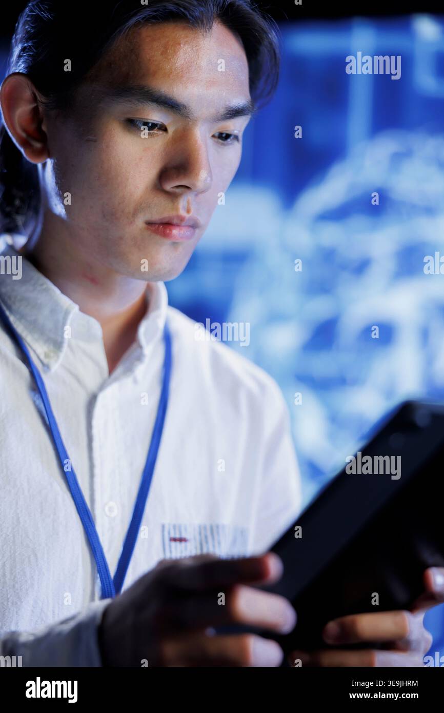 Computer scientist using tablet in data center to maintenance artificial intelligence neural networks simulating human thought processes in computerized model. Asian man doing checkup on AI systems Stock Photo
