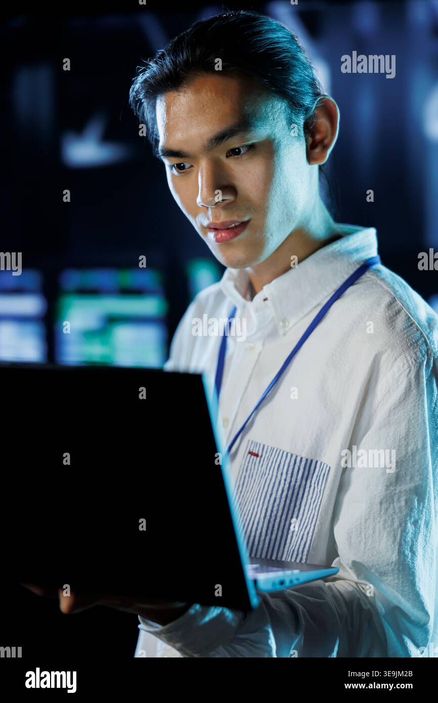 Dara center knowledgeable professional running code and programming on laptop, troubleshooting and upgrading high tech facility designed to accommodate rows of fully operational server electronics Stock Photo