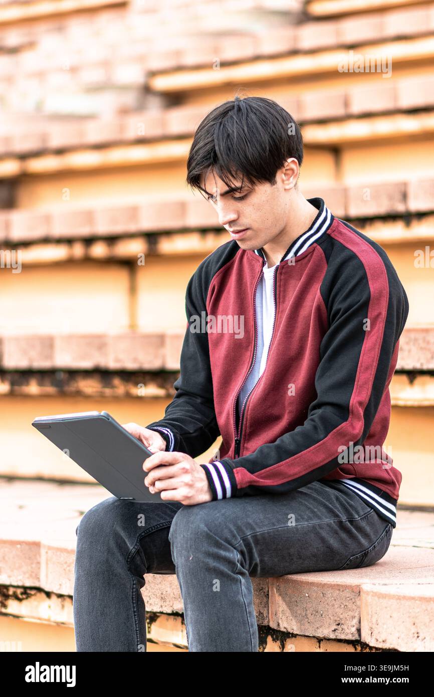 Young student concentrating on tablet sitting on campus stairs Stock Photo