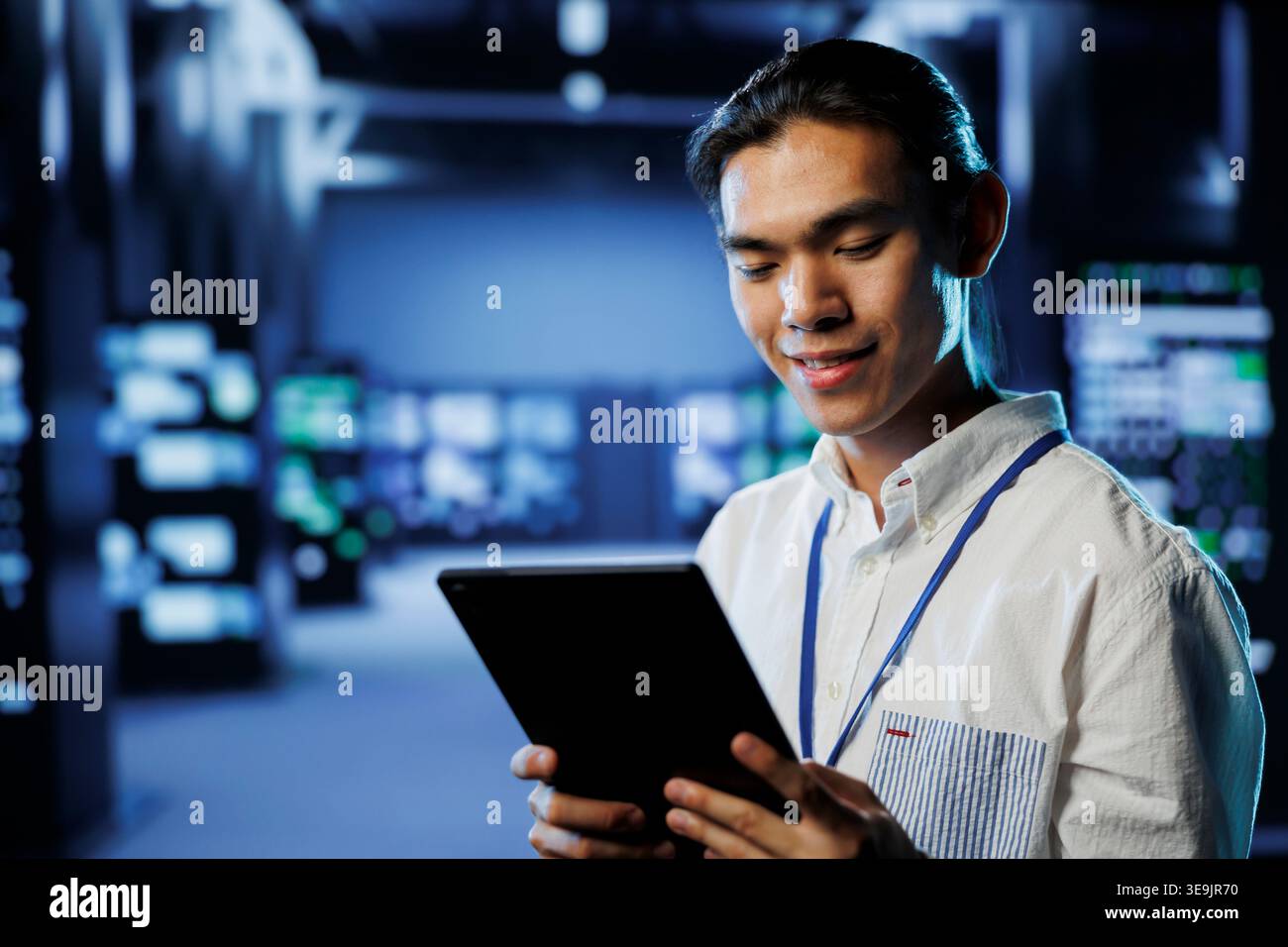 Cheerful computer operator in data center uses tablet to prevent system overload during peak traffic periods. BIPOC man in server facility ensuring enough network bandwidth for smooth operations Stock Photo