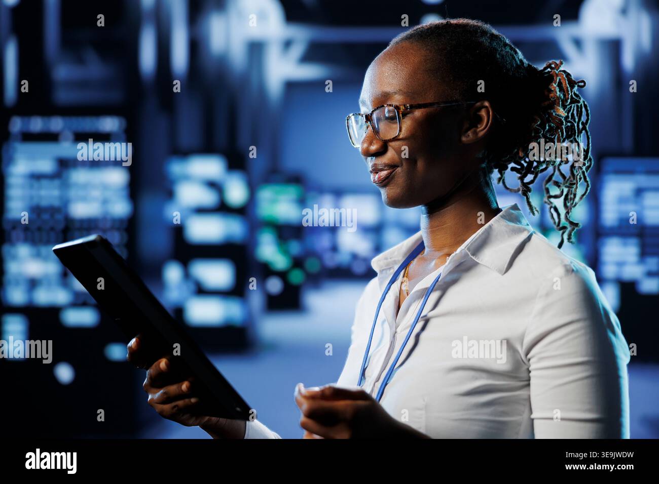 Upbeat admin in data center uses tablet to prevent system infrastructure overload. Precise expert between blade servers ensuring enough network bandwidth for smooth operations Stock Photo