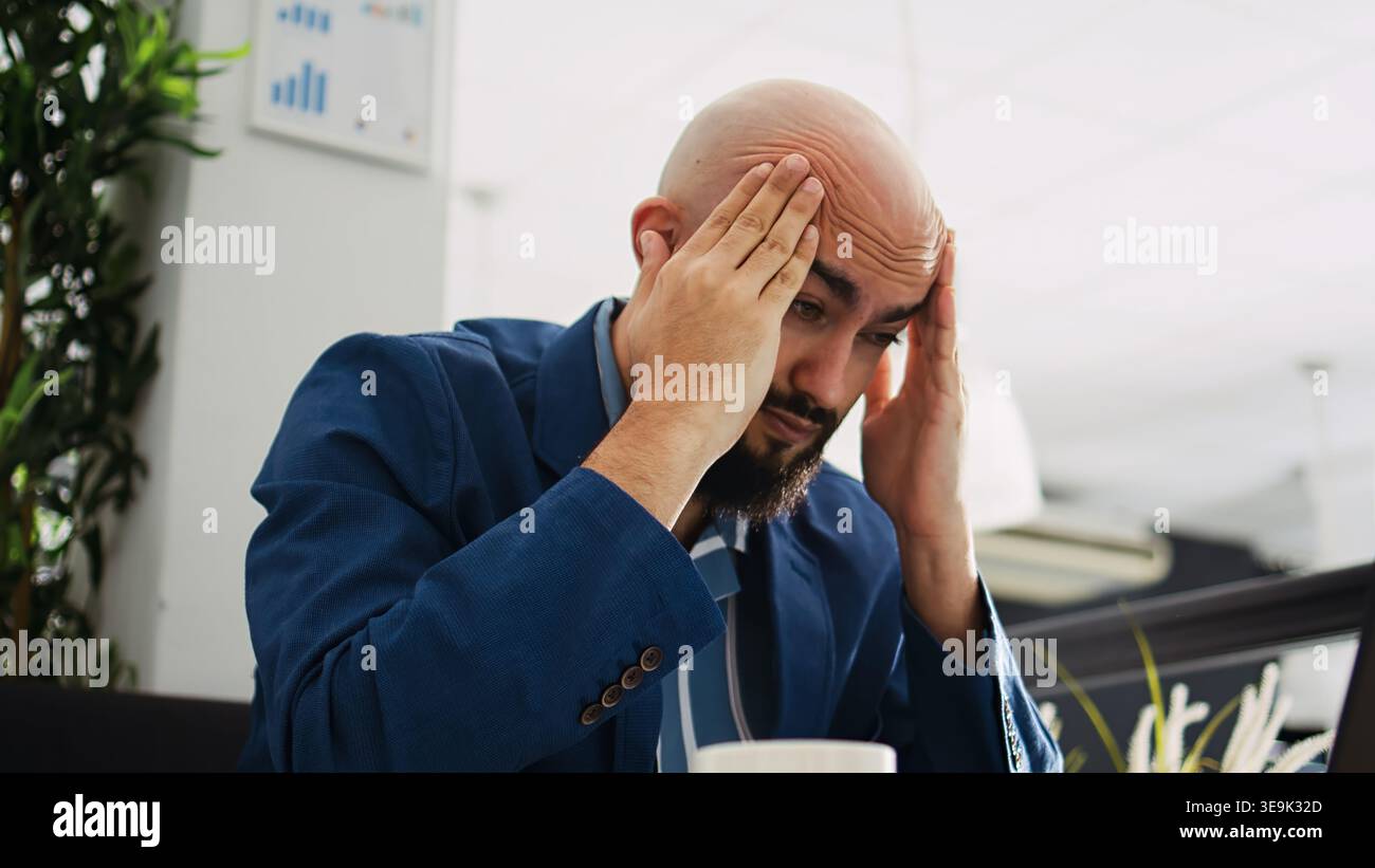 Burnout in coworking space. Businessman being tired and having migraine at work, trying to develop new ideas for startup improvement. Unwell overworked employee dealing with headache. Tripod shot. Stock Photo