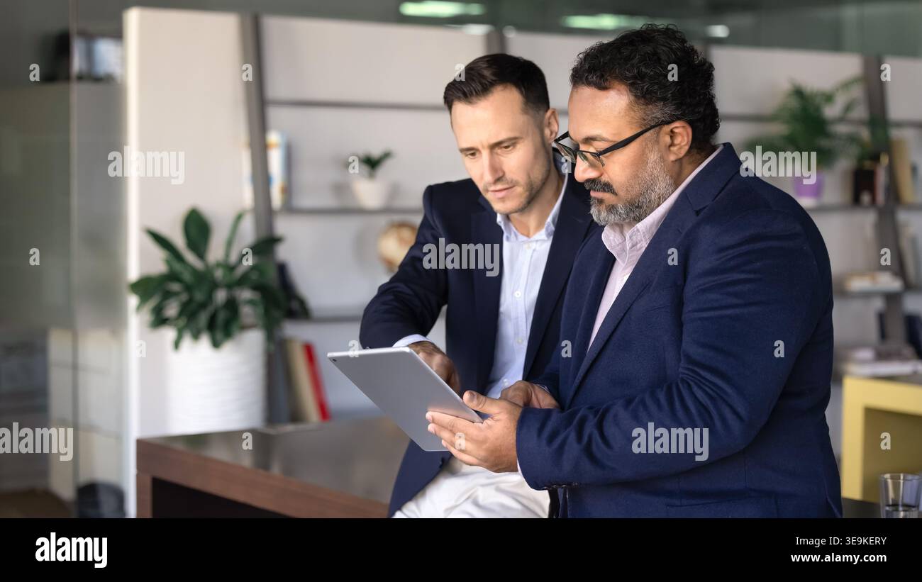 Two focused professionals using tablet working together on digital tasks Stock Photo