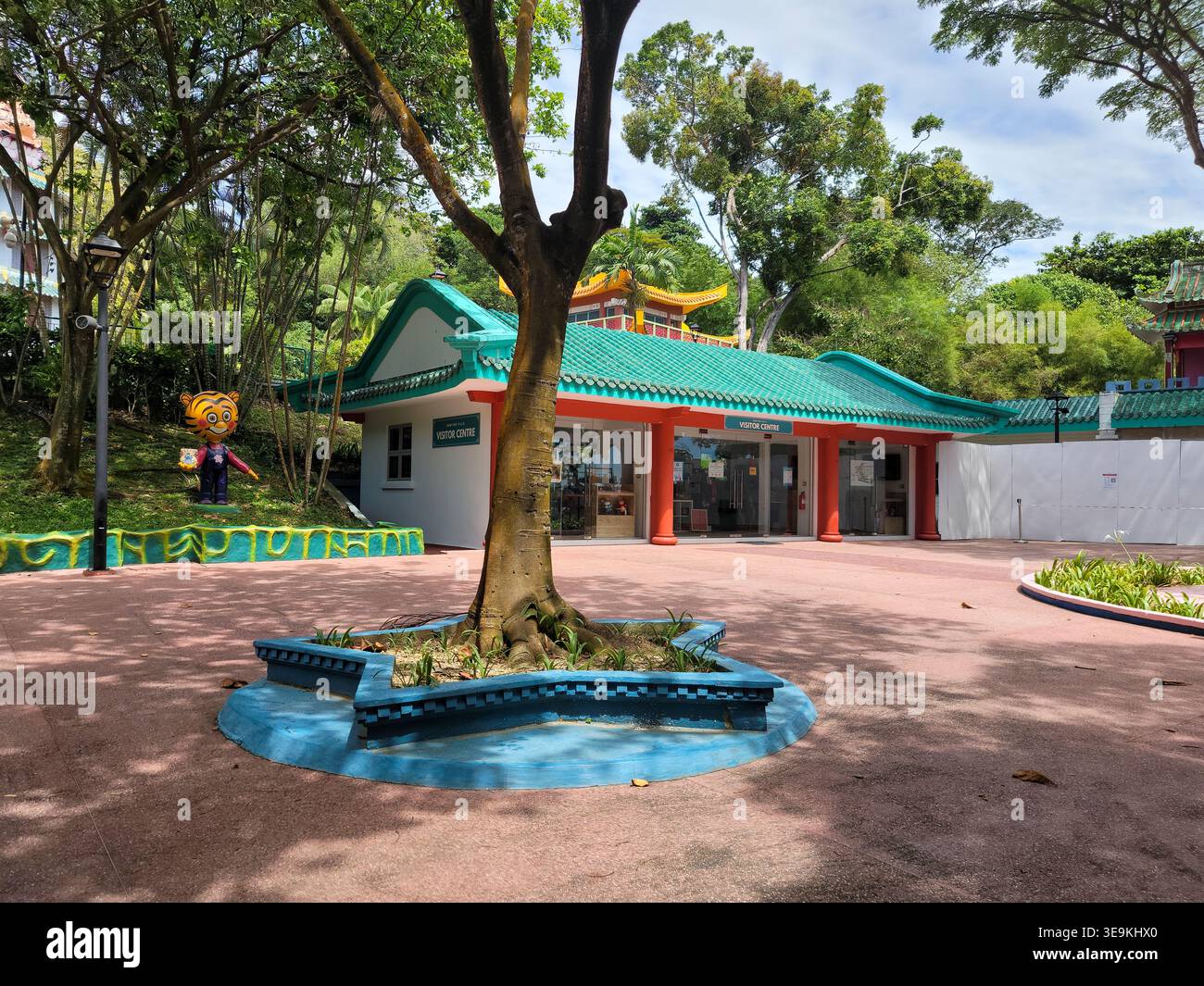 Green-tiled building with red pillars stands beneath a tree. Tree roots ...