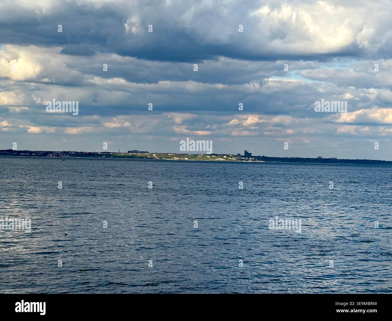 Distant City Skyline and Moody Ocean View Under Dramatic Cloudscape Stock Photo