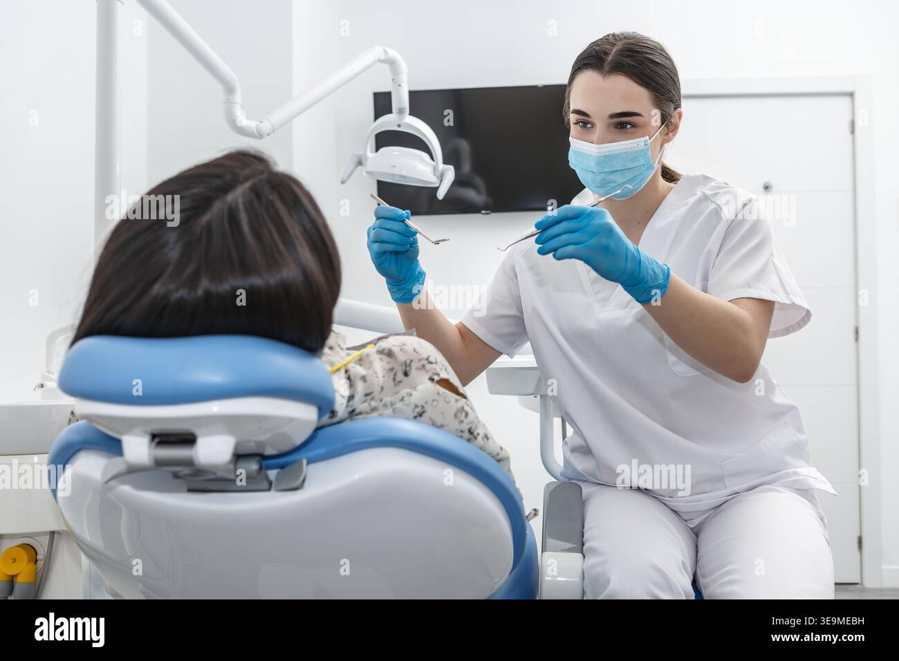 A dentist in a dental clinic is explaining a dental procedure to a patient sitting in a dental chair. Stock Photo