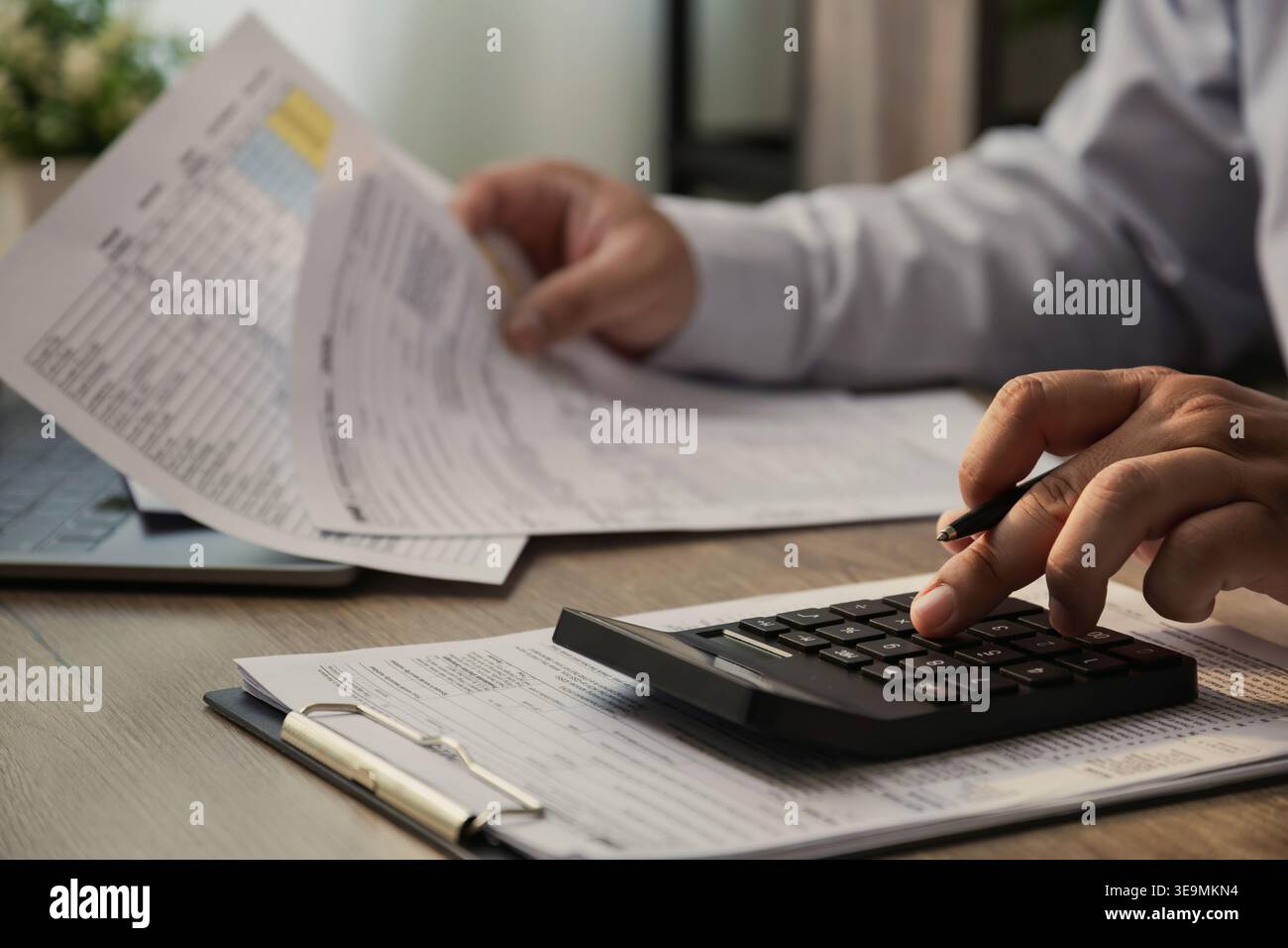 Close up of businessman using calculator and reviewing financial documents on desk, analyzing business report, accounting data, and tax paperwork in m Stock Photo