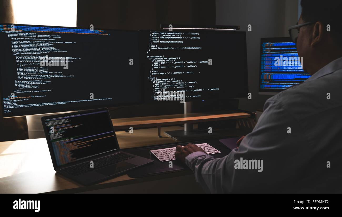 programmer working at a multi monitor computer setup with code on screens in a dark workspace, illustrating software development, coding, debugging, a Stock Photo