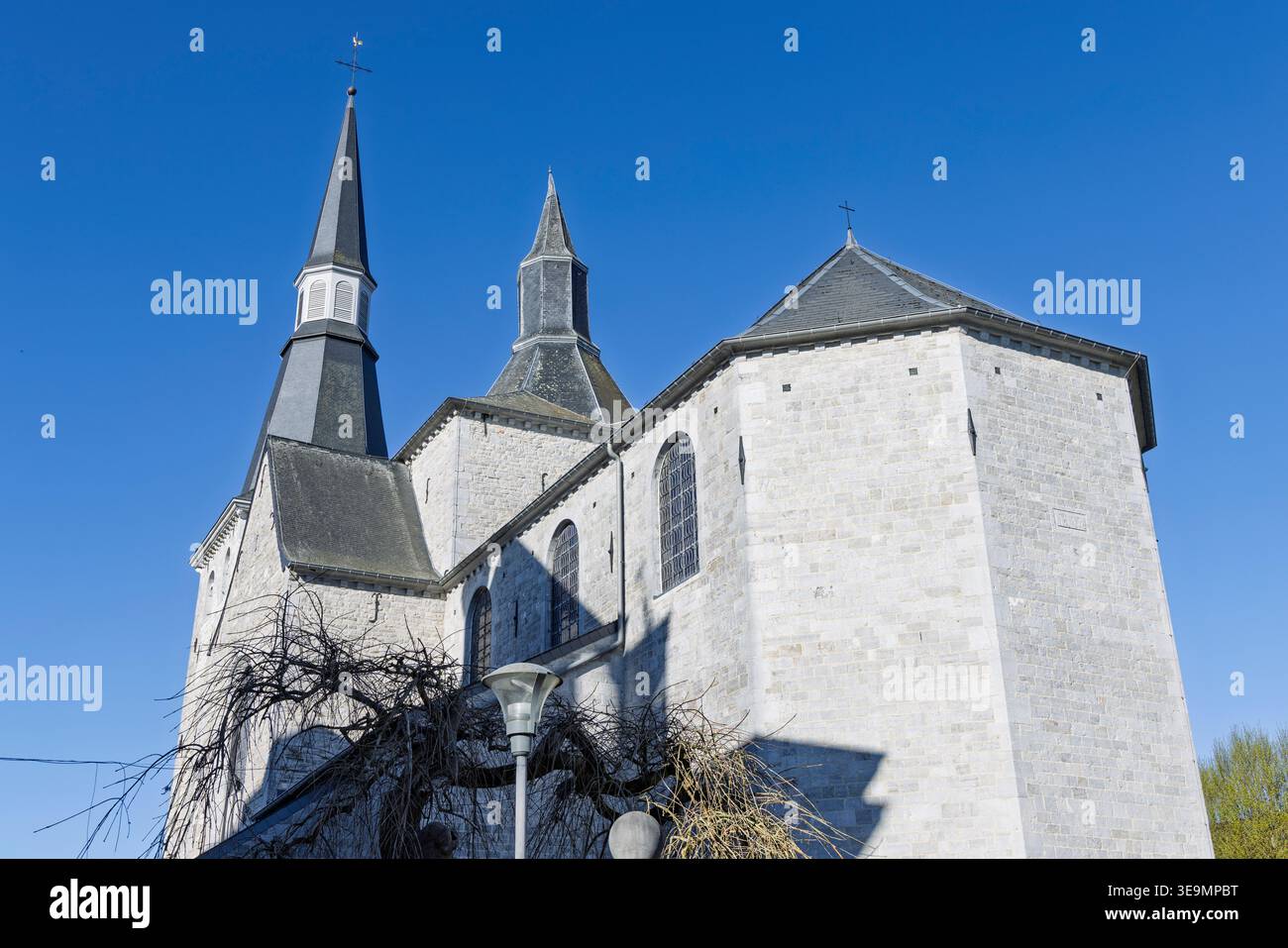 Ciney, Belgium. Detailed view of the stone exterior architecture and grey slate steeples of the town's historic church against a blue sky. Stock Photo