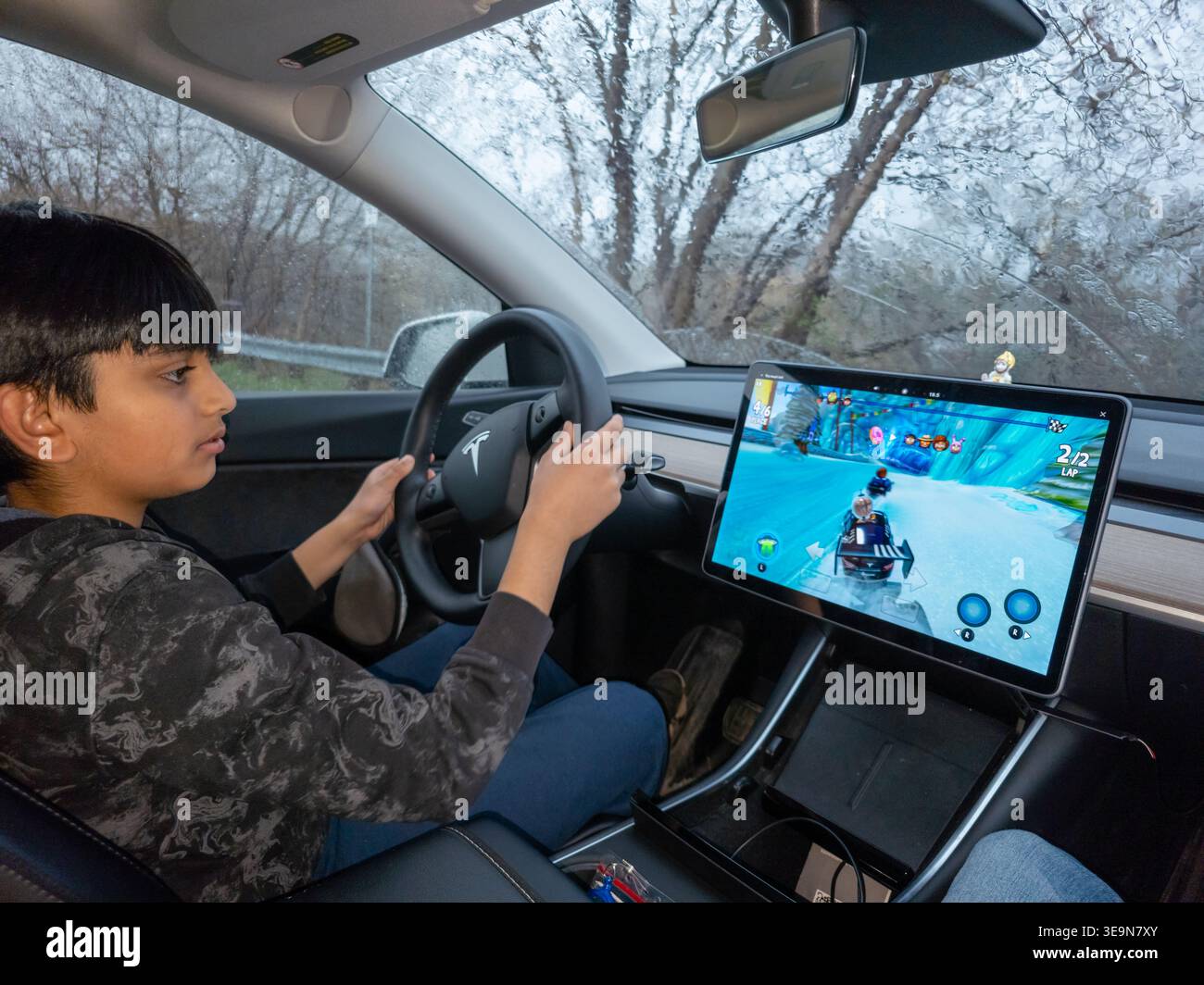 Driver holding the steering wheel of a Tesla while its touchscreen displays an in‑car video game, highlighting EV entertainmet technology. - Smartphone Captured Stock Image