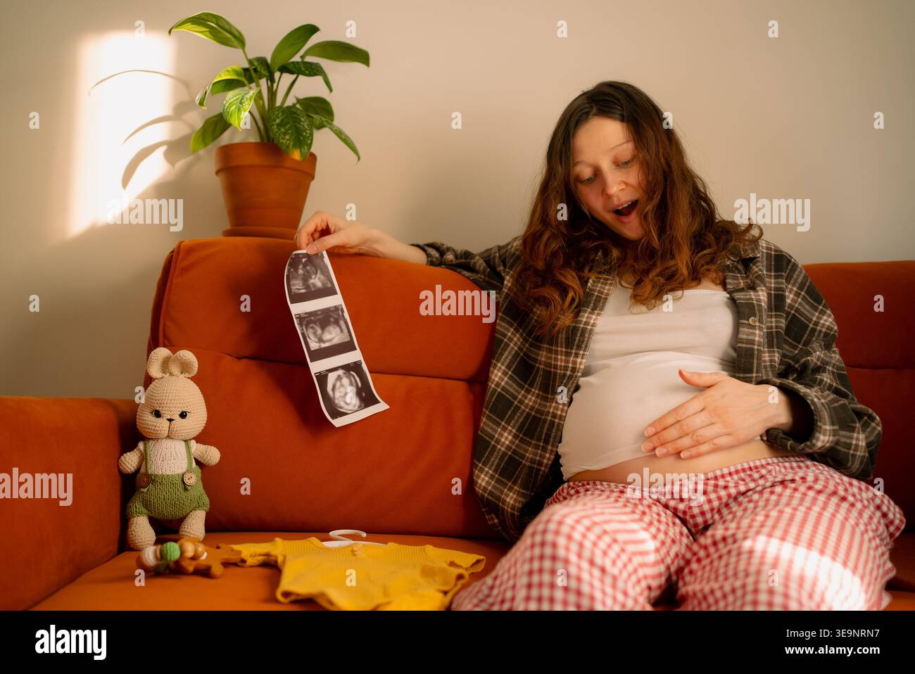 Pregnant woman feeling her stomach and holding ultrasound scans, connecting with her baby and expressing joy and expectation for the new family member while preparing for the arrival at home Stock Photo