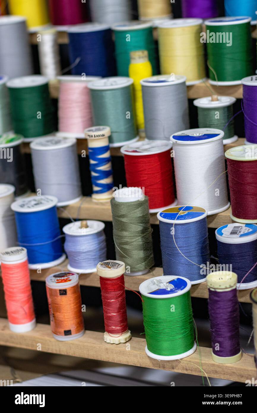 A vibrant display of colorful sewing thread spools neatly arranged on a wooden rack. Perfect for tailoring, crafting, and embroidery projects. Stock Photo