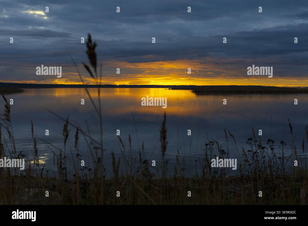 Intense sunset with glowing horizon and dark clouds over still water. Atmospheric coastal scene. Stock Photo