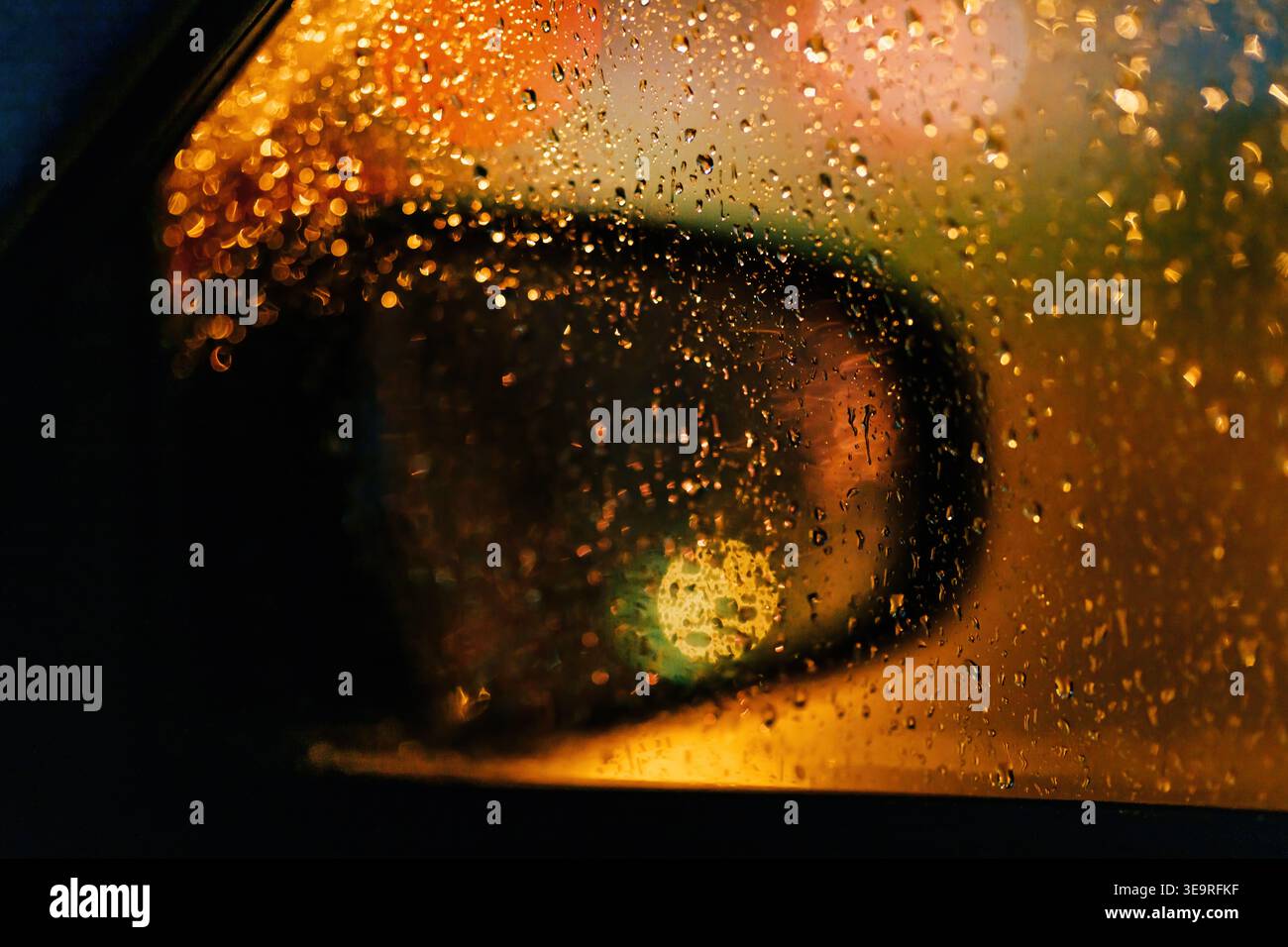 Raindrops on car window and side mirror with city night lights and bokeh reflections, selective focus Stock Photo