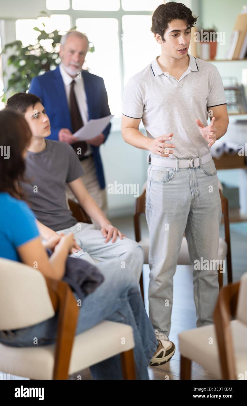 Young guy standing and talking to students sitting in a circle Stock Photo
