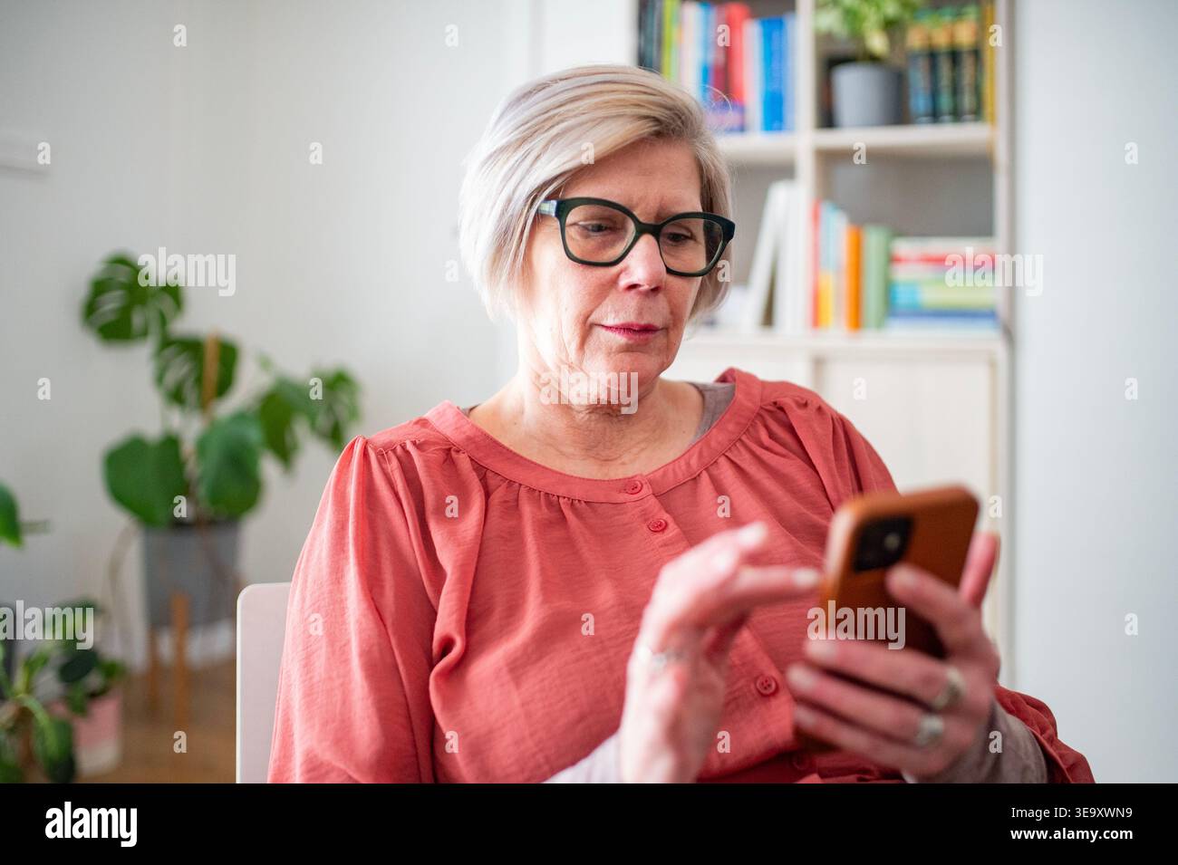 Older woman scrolling on phone while working from home during retirement. Stock Photo