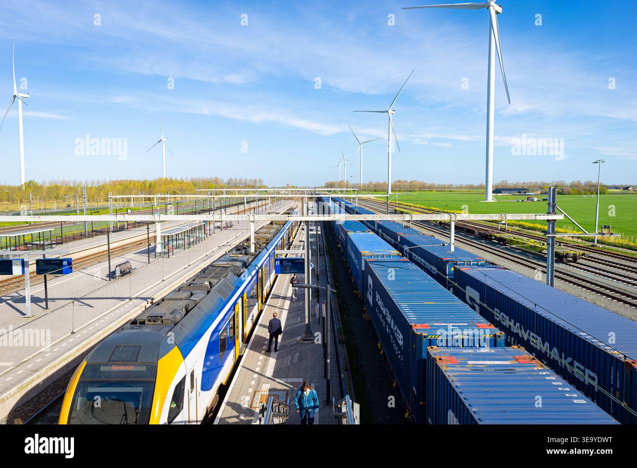 Passenger and freight trains at modern station with wind turbines and green agricultural landscape Stock Photo
