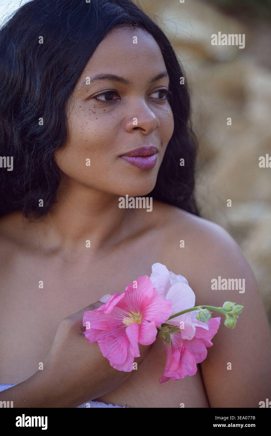 Profile portrait of a young Black woman holding pink mallow flowers Stock Photo