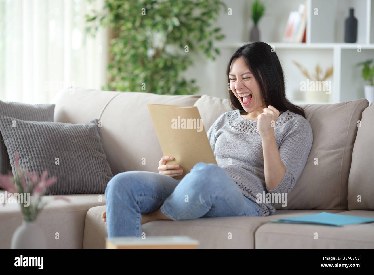 Excited asian woman checking paper documents sitting on a couch at home Stock Photo