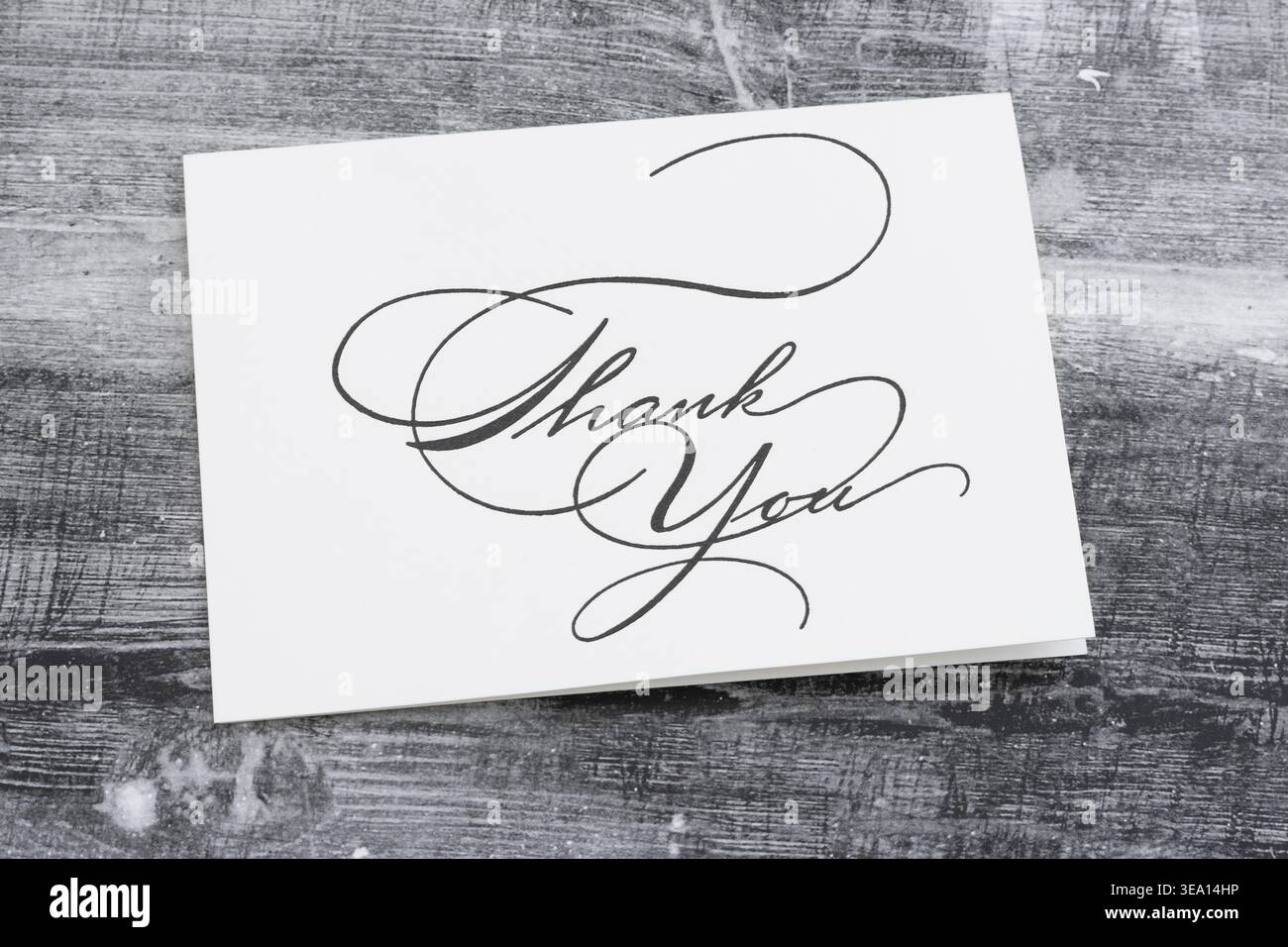 White thank you card with elegant handwritten calligraphy on dark rustic wooden surface, ideal for gratitude, appreciation, and greeting themes Stock Photo