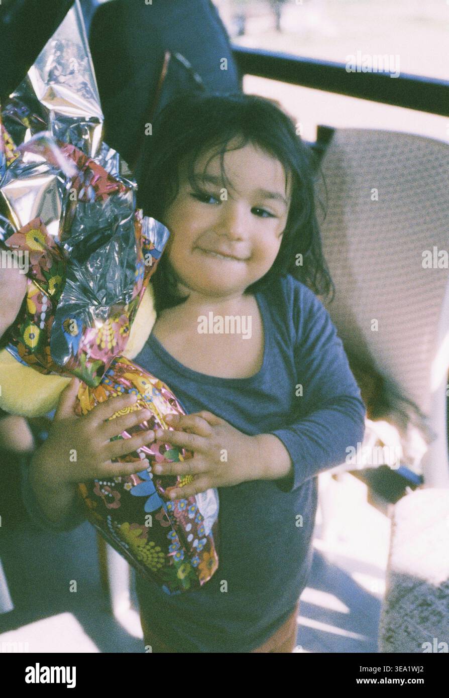 analog film photo of girl holding broken chocolate Easter egg at home. Messy eating and childhood indulgence concept. Copy space for text Stock Photo