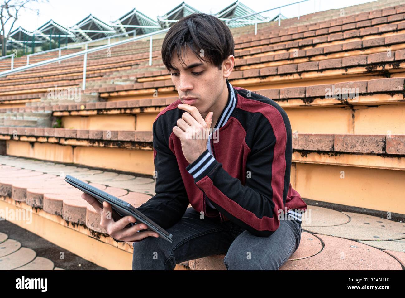 Young man thinking while working on tablet outdoors Stock Photo