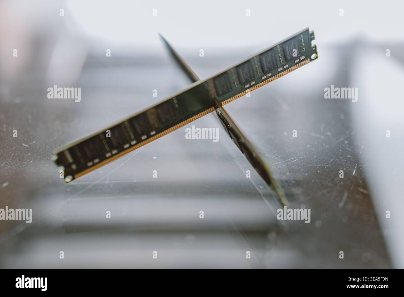 Crossed RAM modules resting on scratched glass surface, close-up tech hardware composition with Stock Photo