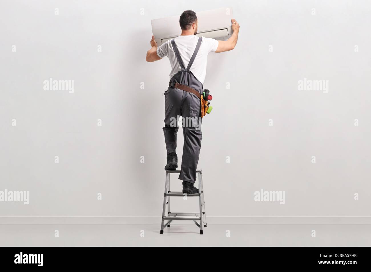 Technician on a ladder installing an air conditioning unit Stock Photo