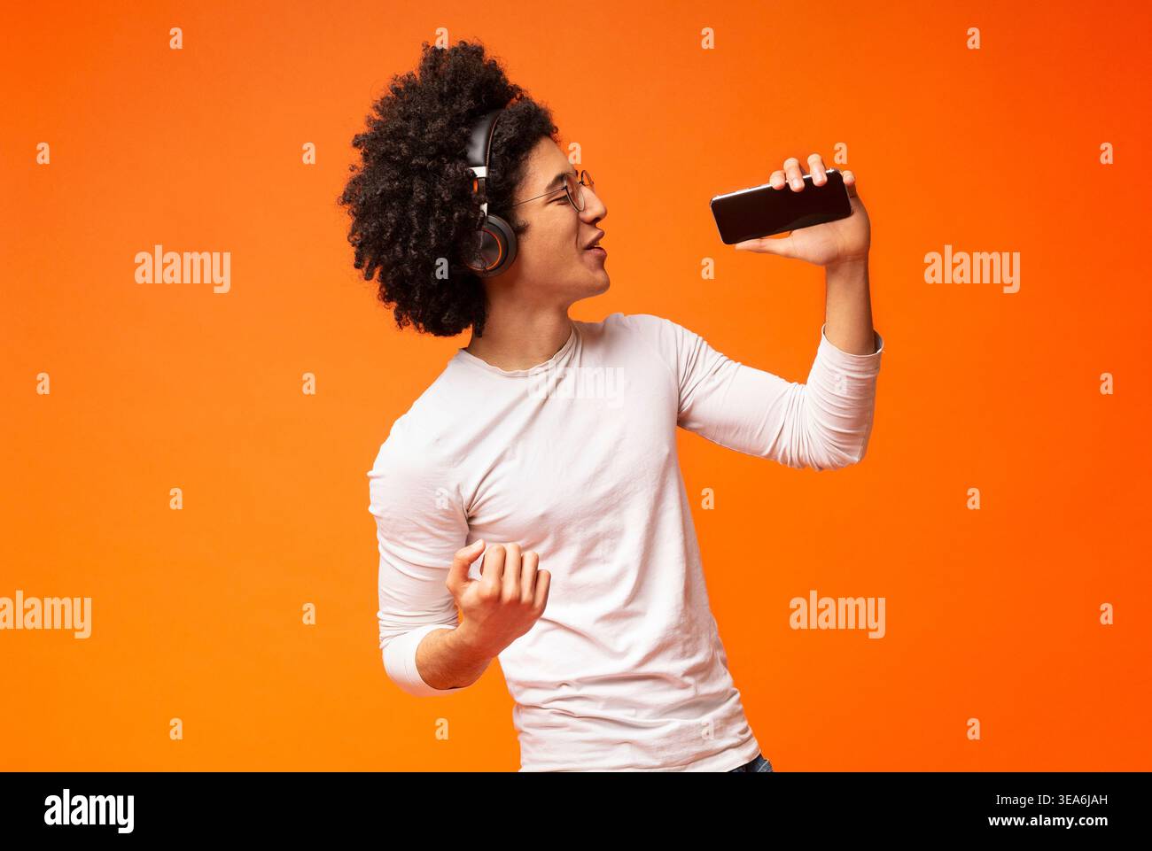 Emotional black guy in wireless headphones singing into phone Stock Photo