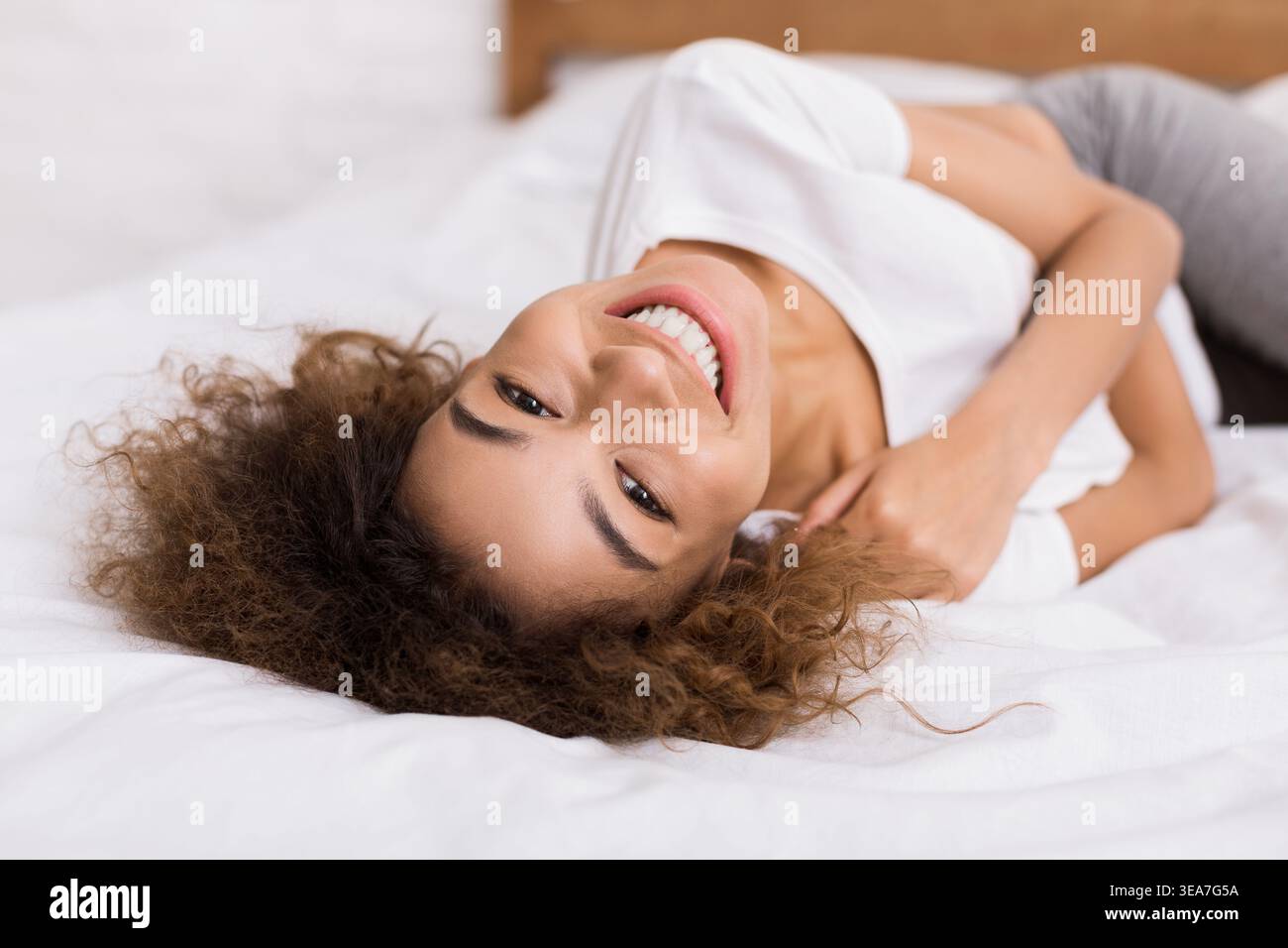 Happy woman lying on bed and looking at camera Stock Photo