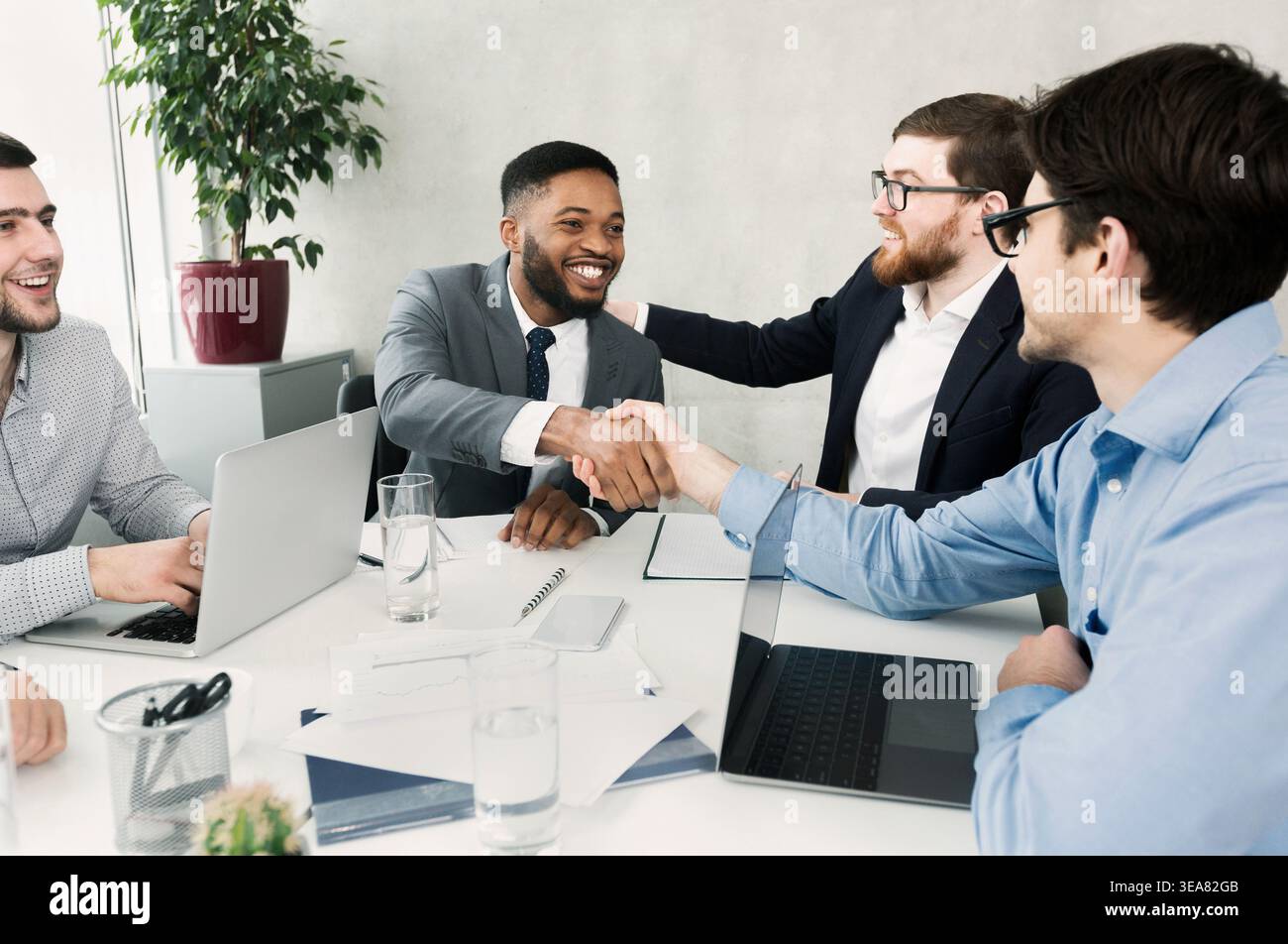 Happy team congratulating successful worker by shaking hands Stock Photo