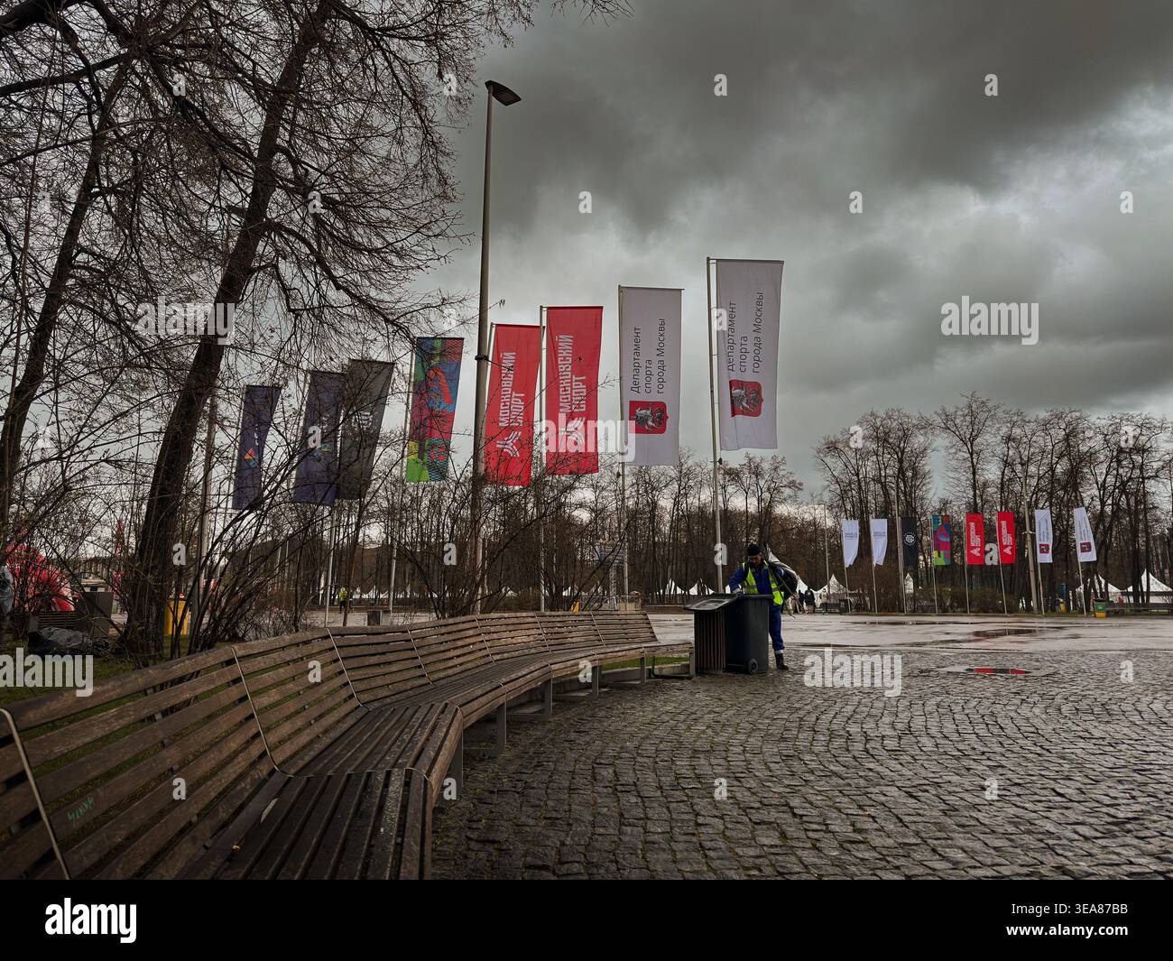 Volunteer waiting by a wooden bench at a local marathon event under a moody, overcast cloudy sky, ready to assist runners. - Smartphone Captured Stock Image