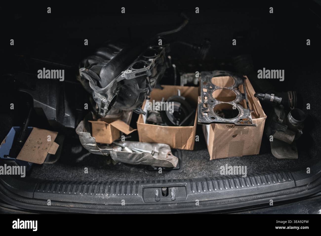 A collection of car parts including an intake manifold, head gasket, and other components are packed inside a car's trunk. The scene captures the tool Stock Photo
