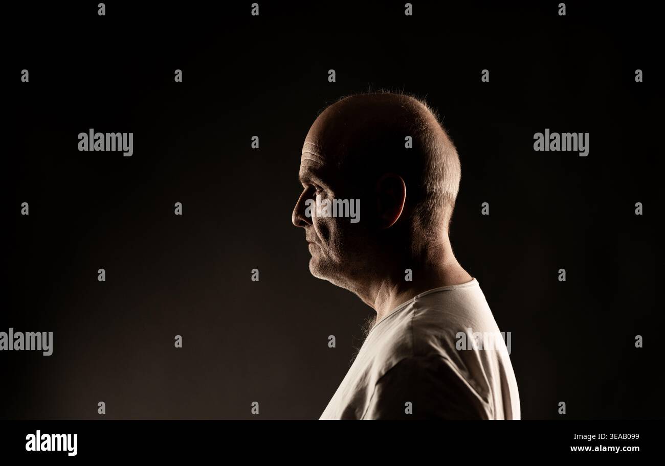 Mature man in profile with dramatic lighting on a dark background Stock Photo