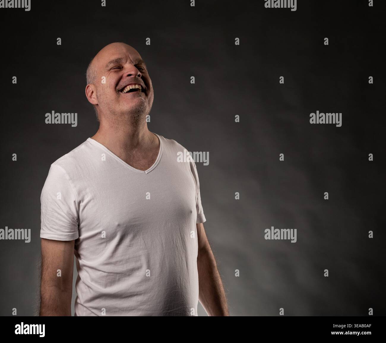 Bald man in white t shirt laughing heartily, expressing strong emotions of joy and glee Stock Photo