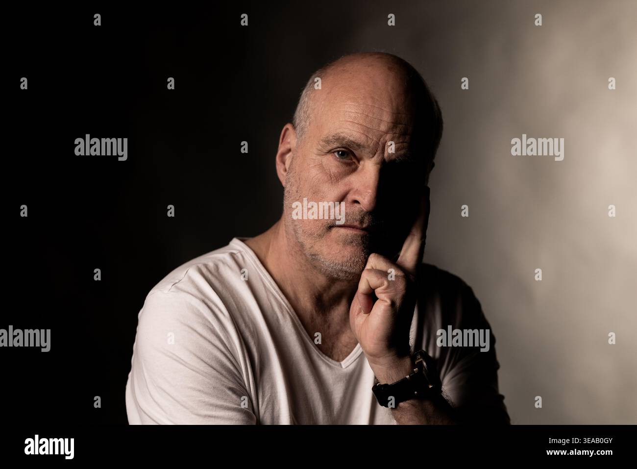 Serious bald man reflecting, thinking deeply against a dark background Stock Photo