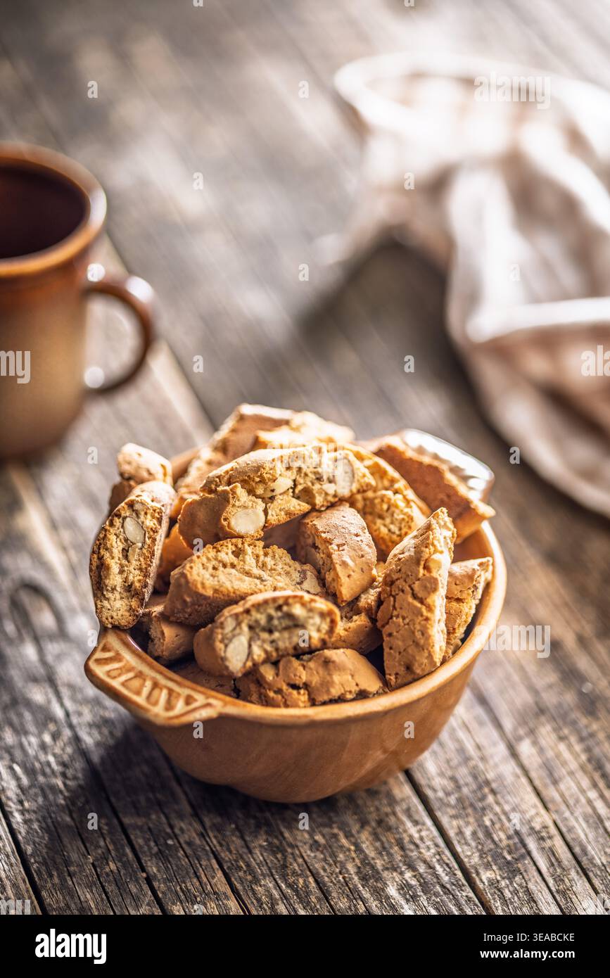 Warm almond biscotti cantuccini piled in a ceramic bowl beside a coffee cup on a rustic wooden table, evoking cozy morning vibes, homemade baking, and Stock Photo
