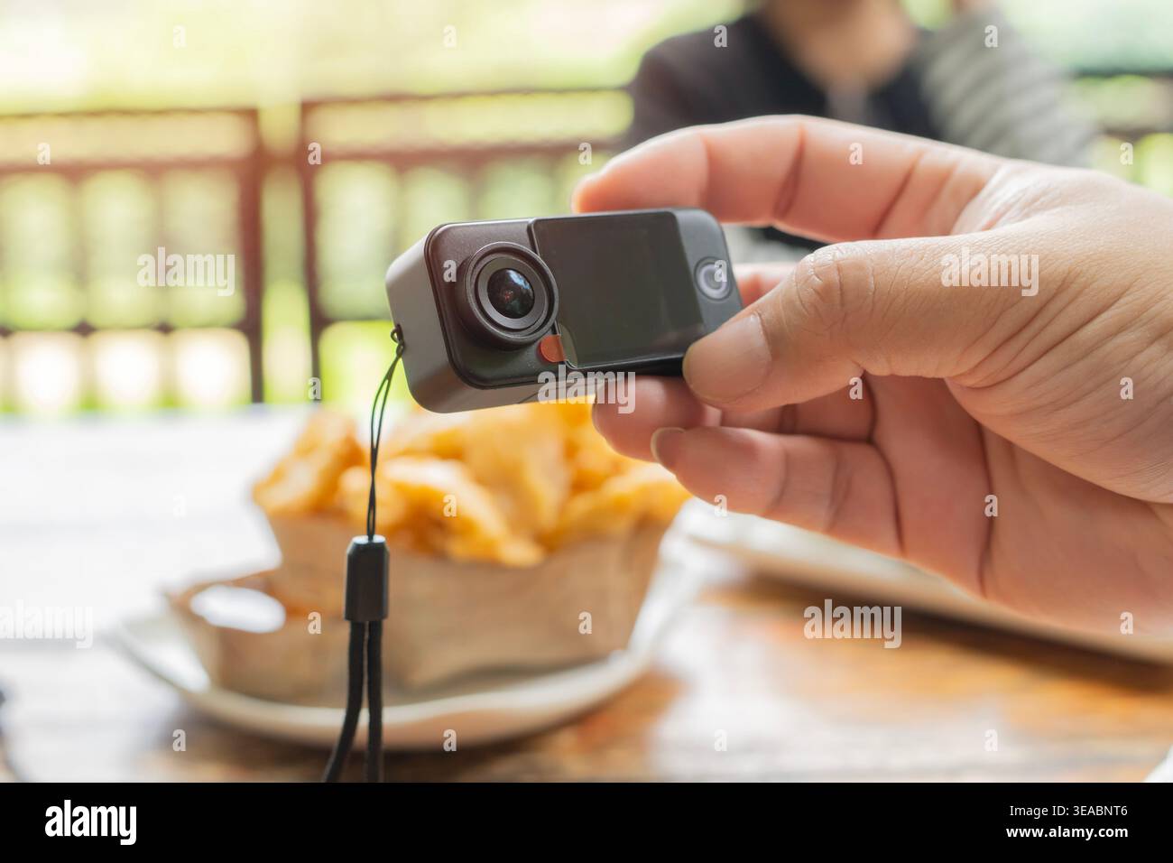 Cropped view close-up of unrecognizable photographer holding mini black action camera while taking pictures of food on table, selective focus. Stock Photo