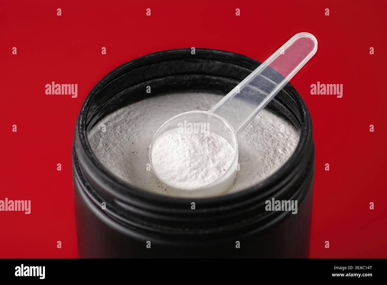 Spoon with creatine proteine in an opened can for sporty lifestyle. Elevated view isolated on red. Stock Photo