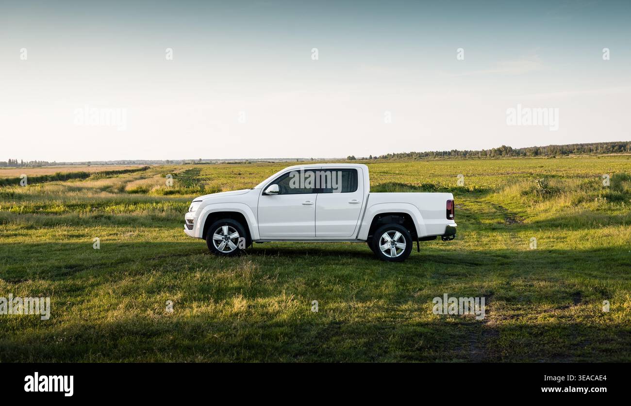 White four-door pickup truck in a summer field. Side profile view of white crew cab truck in a lush green meadow under a clear, late afternoon sky. Stock Photo
