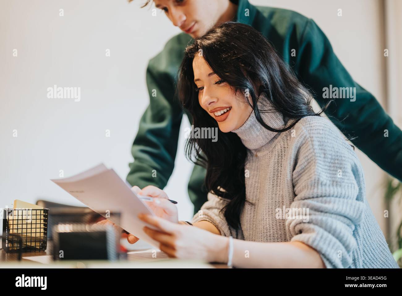 Two students studying together at a desk smiling while reviewing documents and collaborating Stock Photo