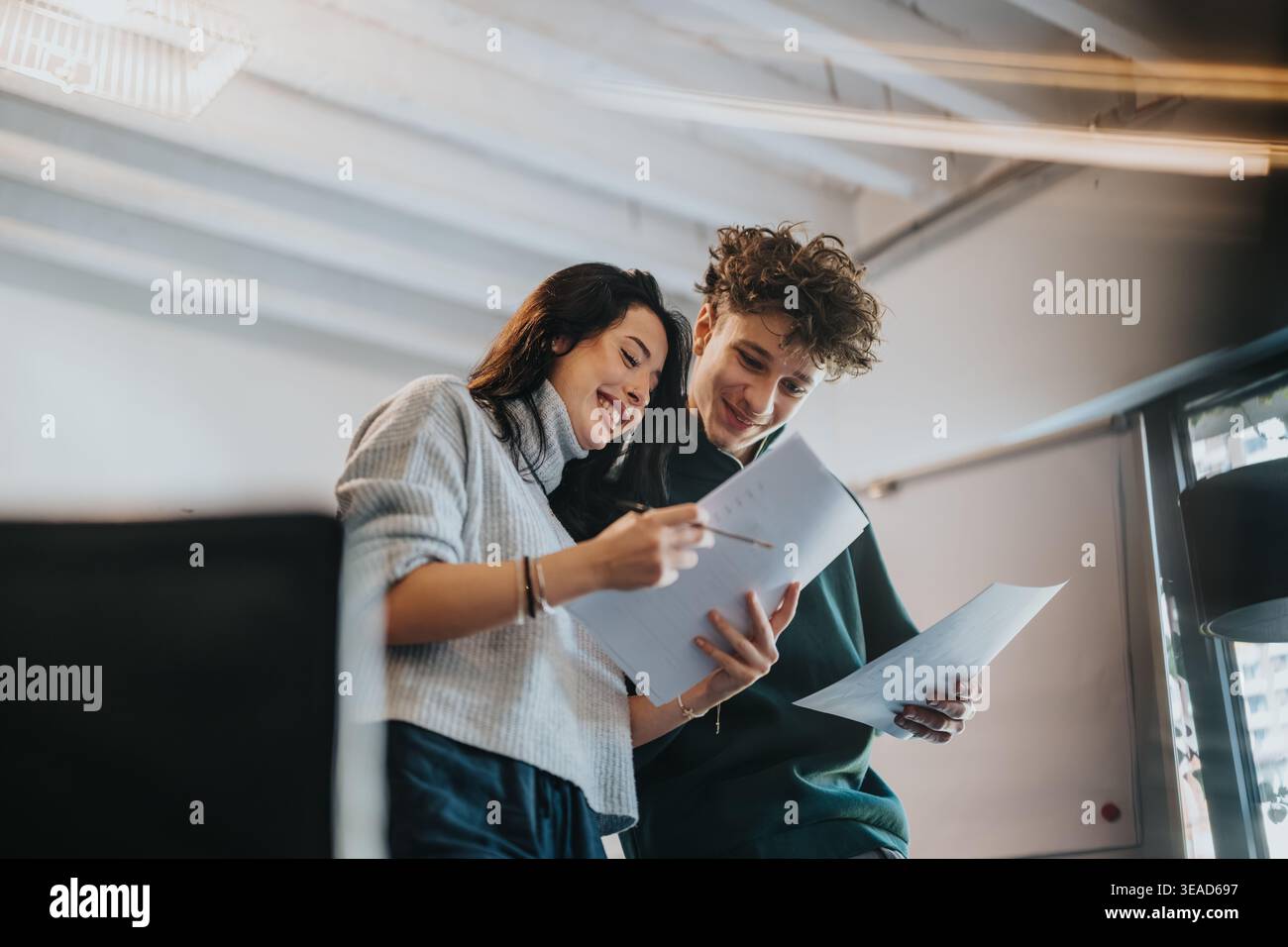 Two students reviewing papers together and smiling while collaborating in a modern study space Stock Photo