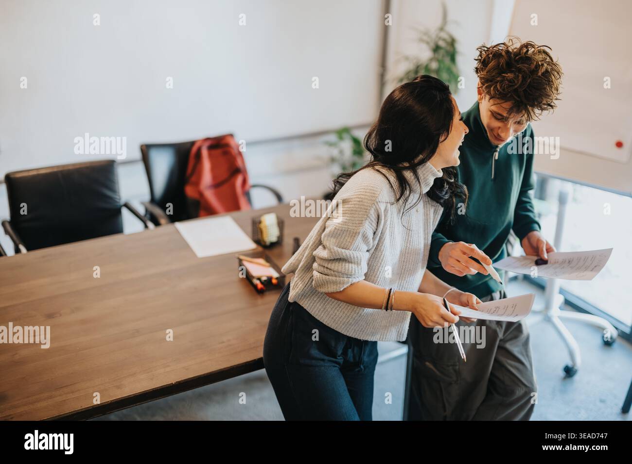 Two students collaborating and smiling over papers in a casual meeting room Stock Photo